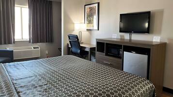 Una habitación de hotel con cama, escritorio, silla, televisor y ventana con cortinas.