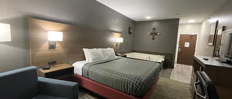 A hotel room with a large bed, a desk with a chair, a TV, and a bathroom with a bathtub.
