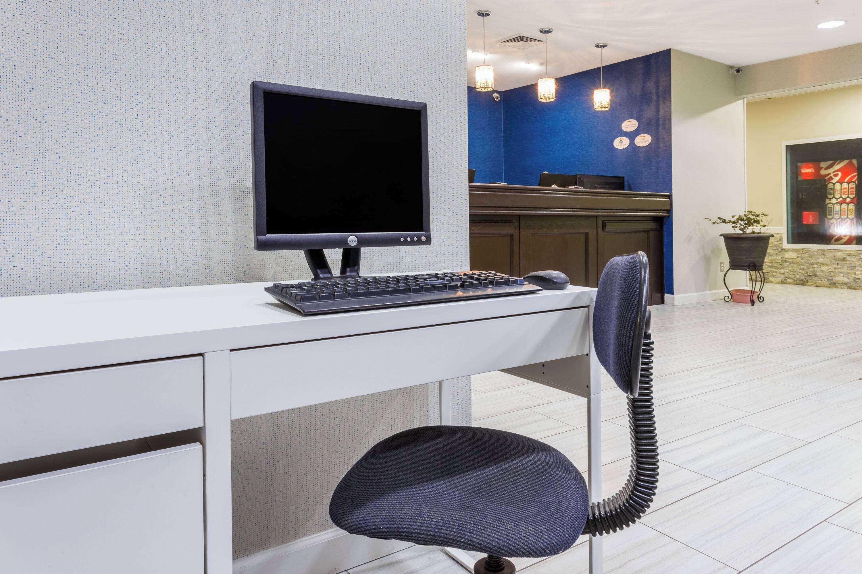 A reception desk with a computer, a chair, and a blue wall with a plant.