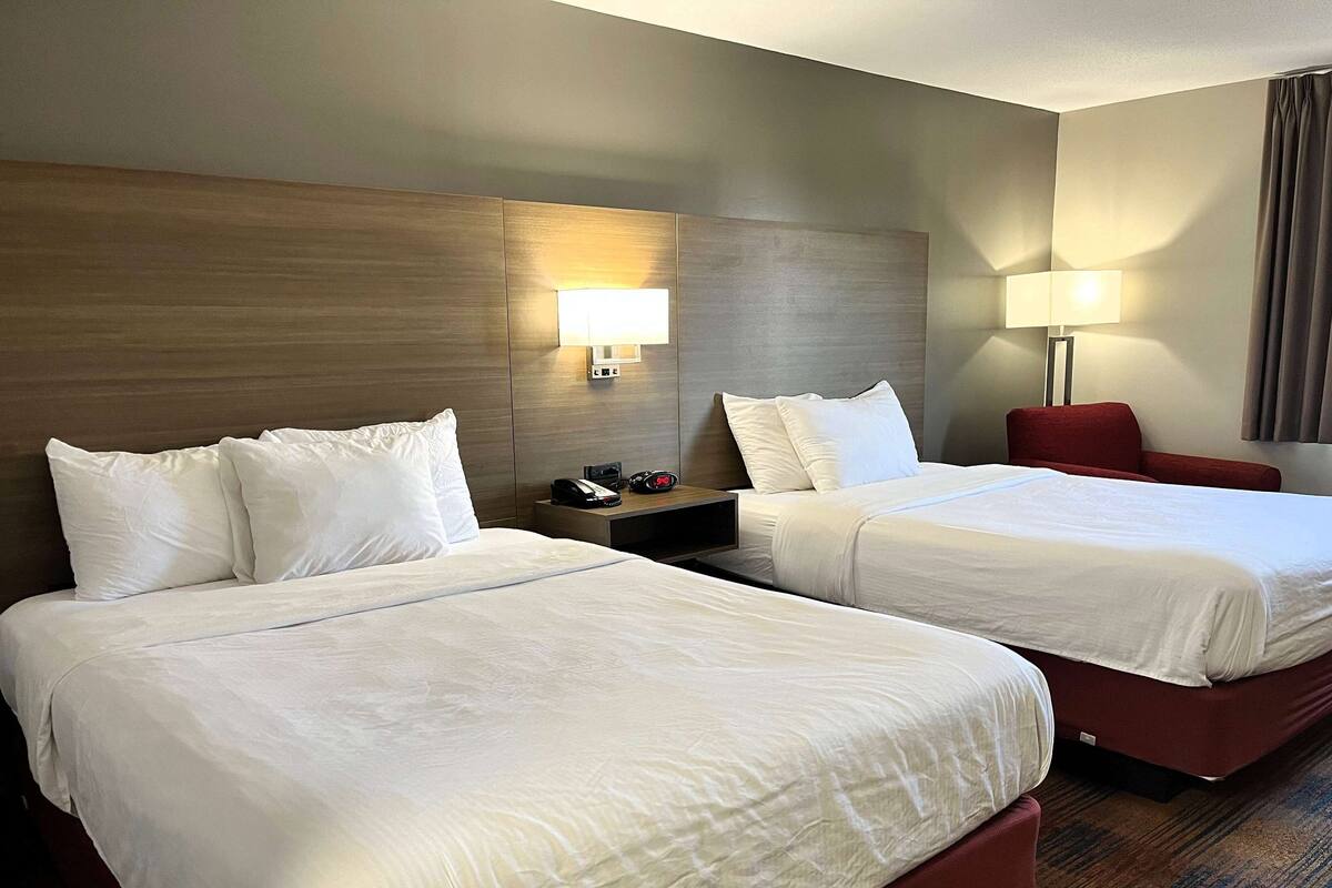 Una habitación de hotel con dos camas, una mesita de noche con lámpara y una silla roja.
