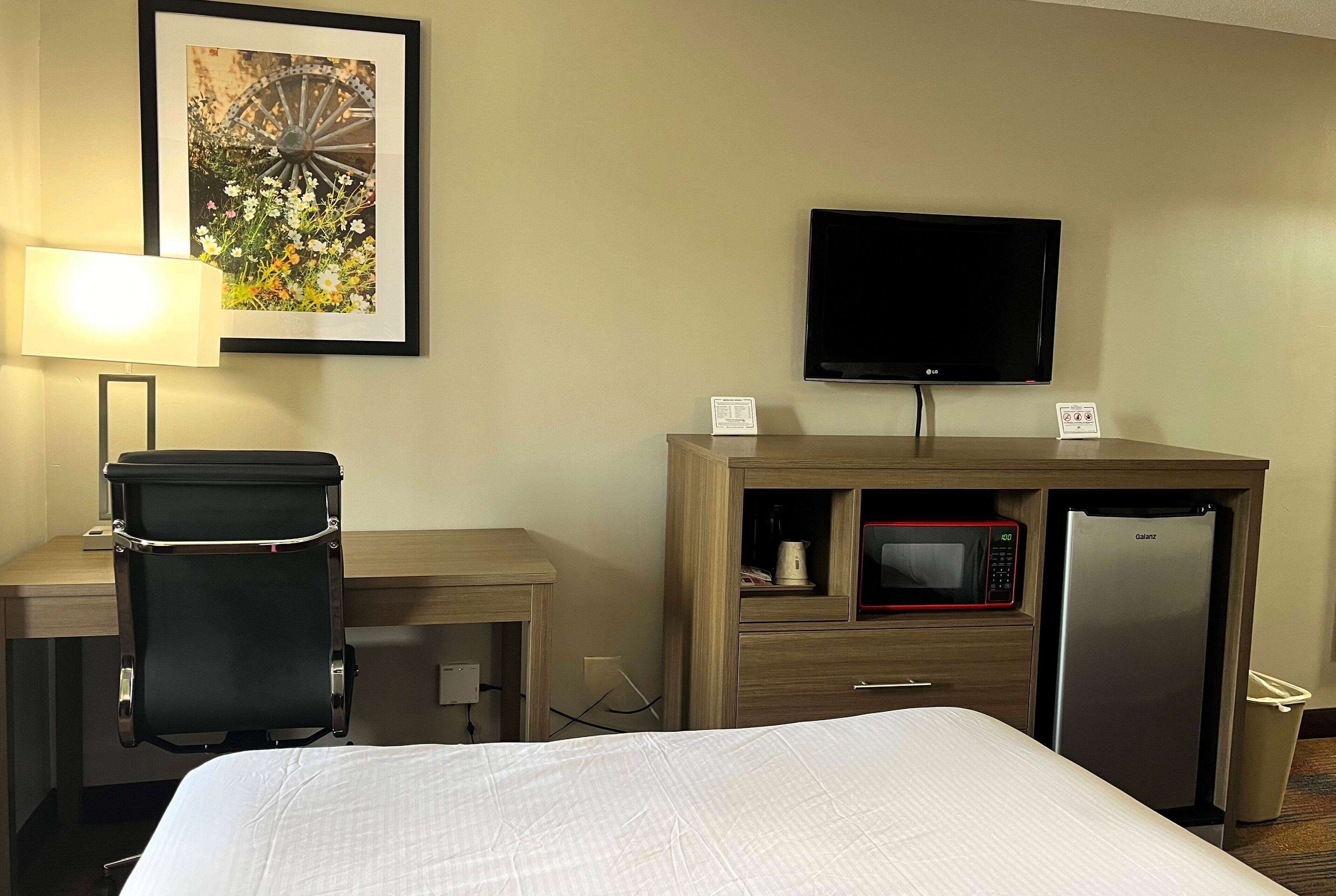 Une chambre d’hôtel équipée d’un lit, d’un bureau avec une chaise, d’une télévision, d’un four à micro-ondes et d’un réfrigérateur.