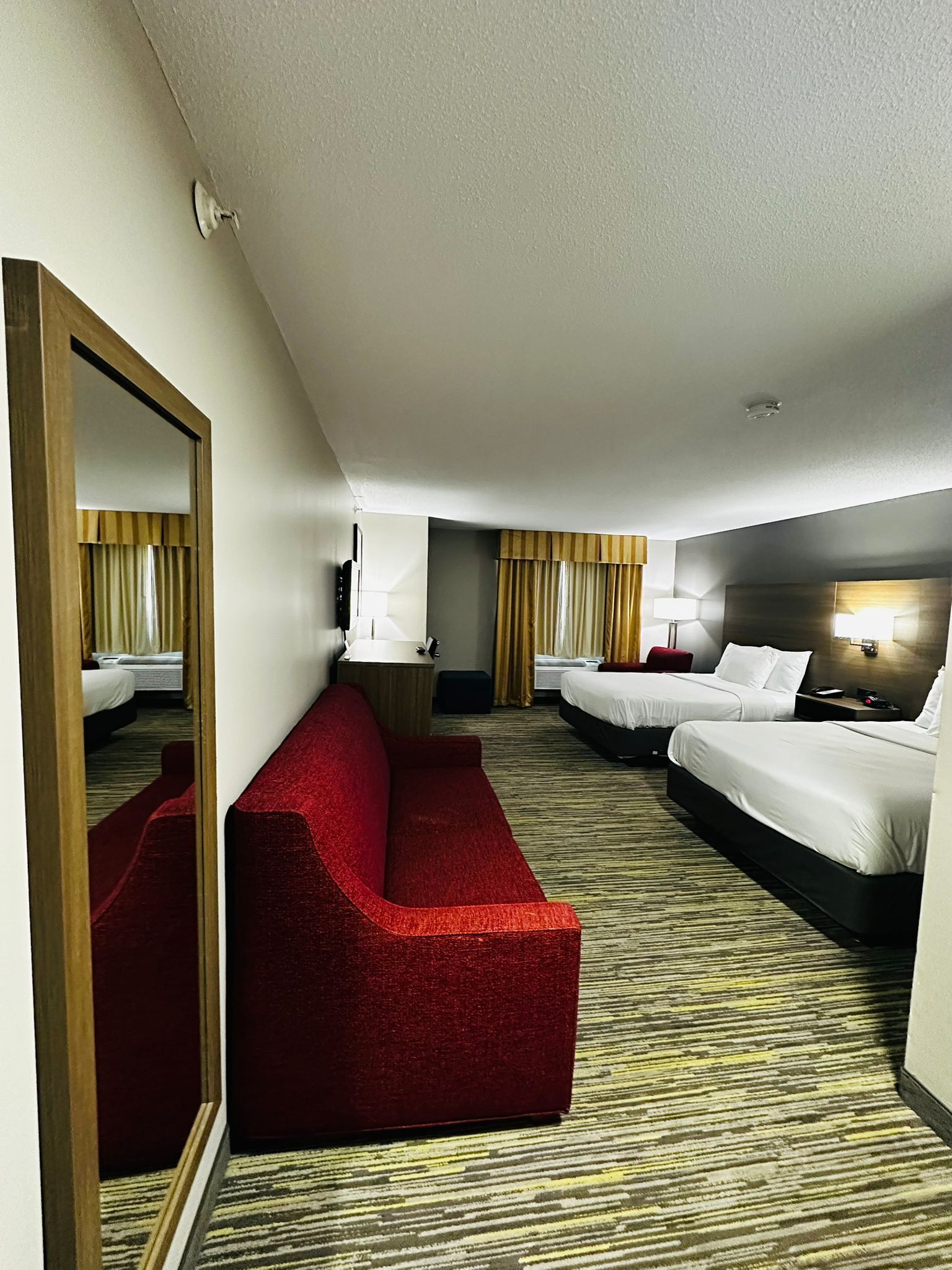 Habitación de hotel con un sofá rojo, dos camas, un espejo y suelo alfombrado.