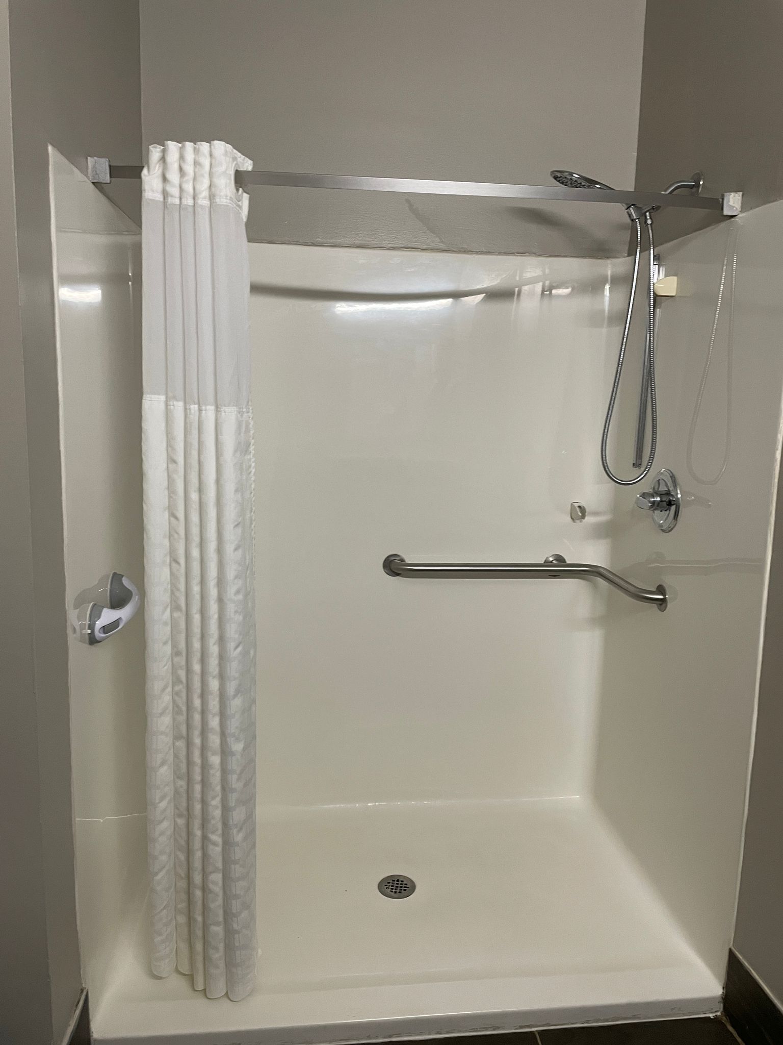 A walk-in shower with a glass door, a showerhead, a handheld shower attachment, and a grab bar.