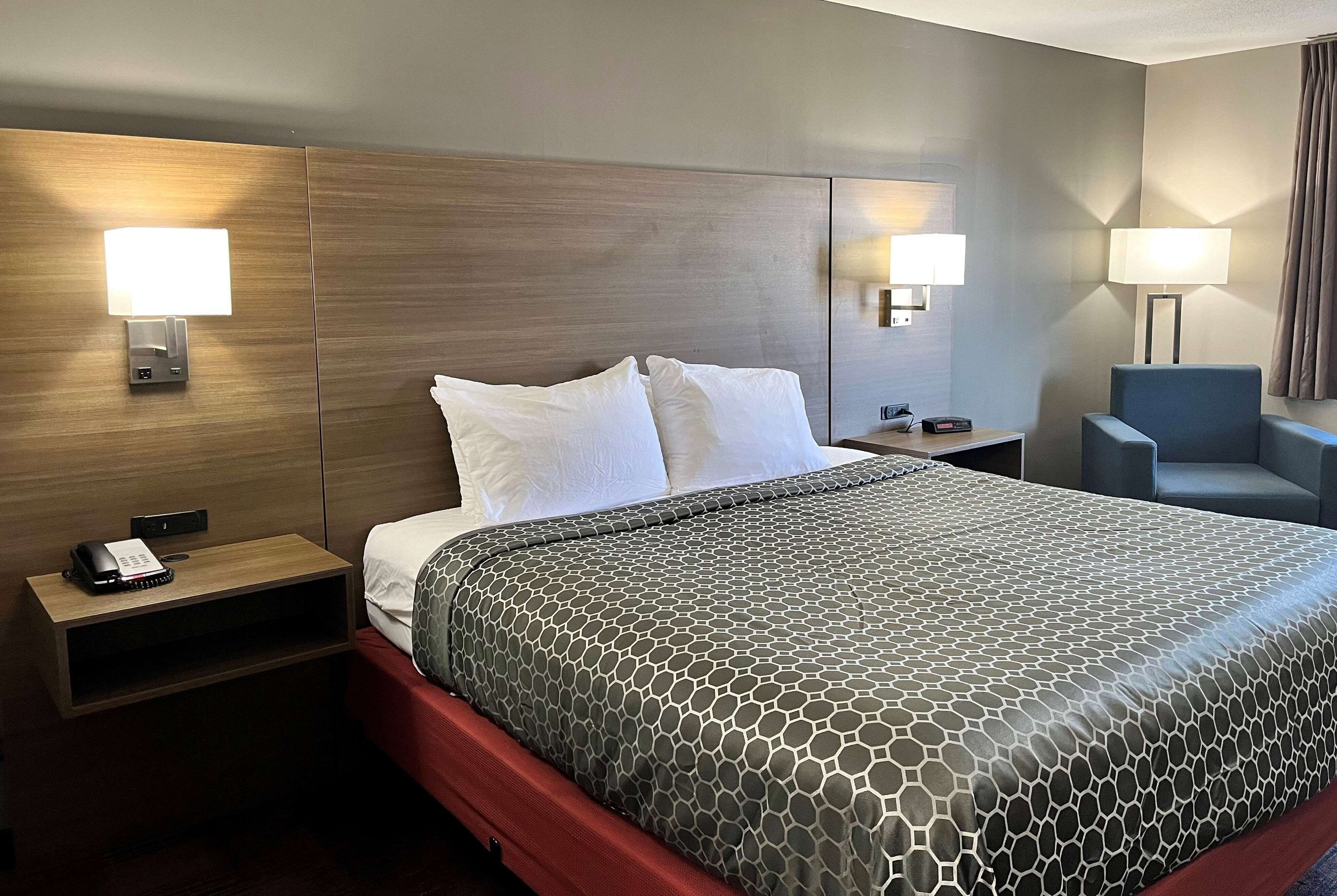 A hotel room with a large bed, two bedside lamps, a desk with a phone, and a chair.