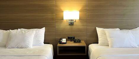 A hotel room with two beds, a bedside table with a phone and a lamp, and a wooden headboard.