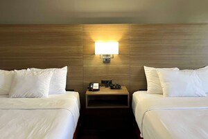 Habitación de hotel con dos camas, una mesita de noche con teléfono y lámpara, y cabecera de madera.