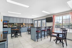 A modern kitchen with grey cabinets, a central island with bar stools, and a large window with curtains.