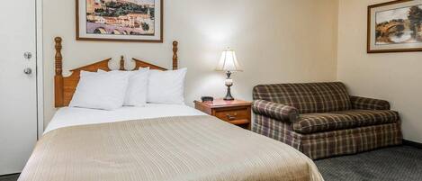 A hotel room with a bed, a chair, a nightstand, and two framed pictures on the walls.