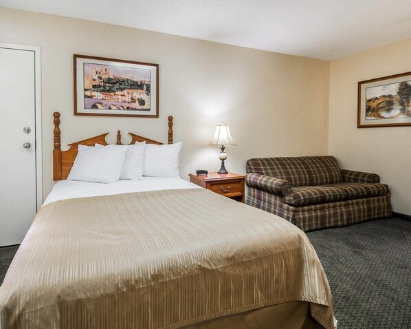 A hotel room with a bed, a chair, a nightstand, and two framed pictures on the walls. - Quality Inn Bainbridge (Bainbridge)