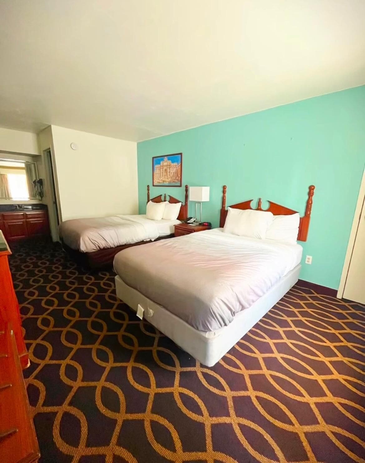 A hotel room with two beds, a bathroom, and a patterned carpet.