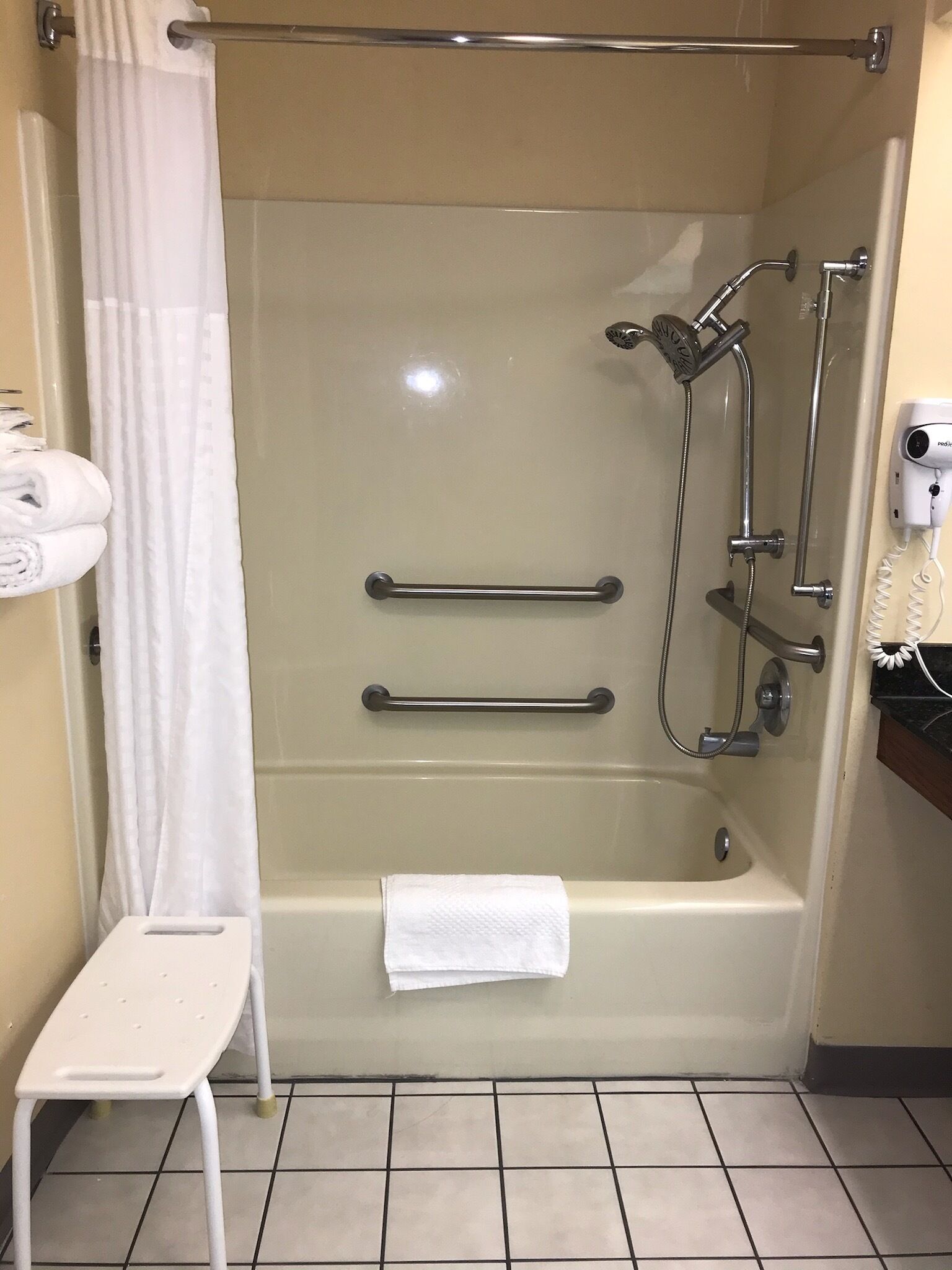Une salle de bain dotée d’une douche à parois de verre, d’un porte-serviettes, d’un pommeau de douche à main et d’un sèche-cheveux fixé au mur.