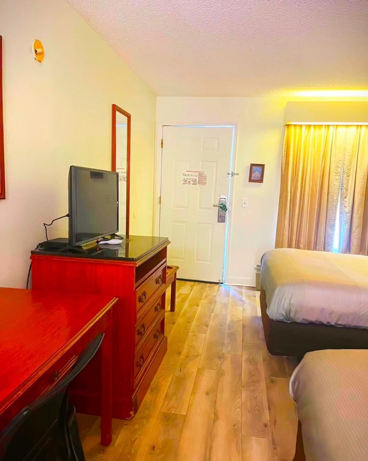 Ein Hotelzimmer mit einem hölzernen Schreibtisch, einem Fernseher, einer Kommode, einem Bett und einer Tür.