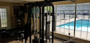 Un gimnasio con equipo de ejercicio y vista a una piscina.