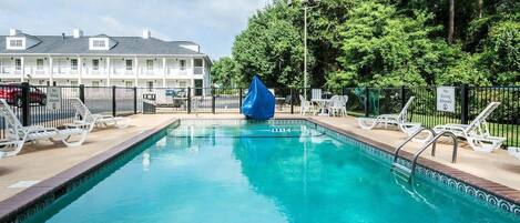 A swimming pool with a no diving sign, surrounded by lounge chairs and a building in the background.