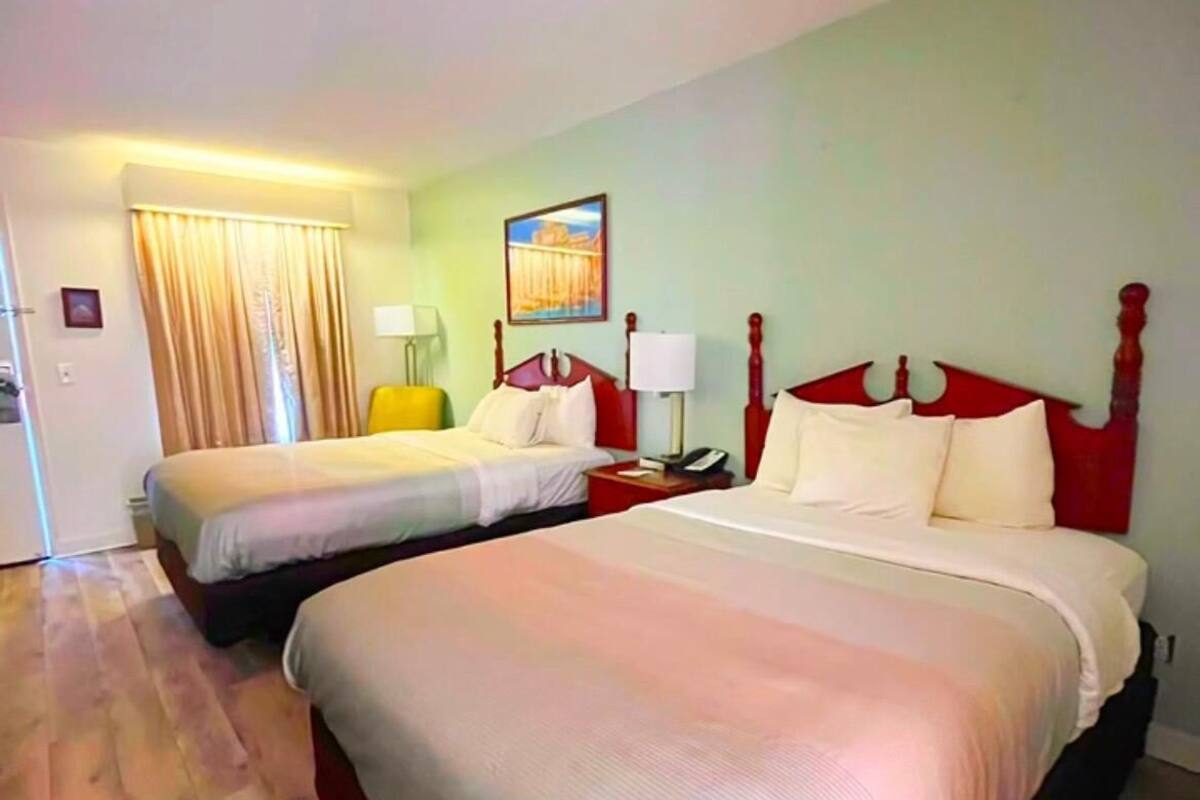A hotel room with two beds, a painting on the wall, and a curtain.