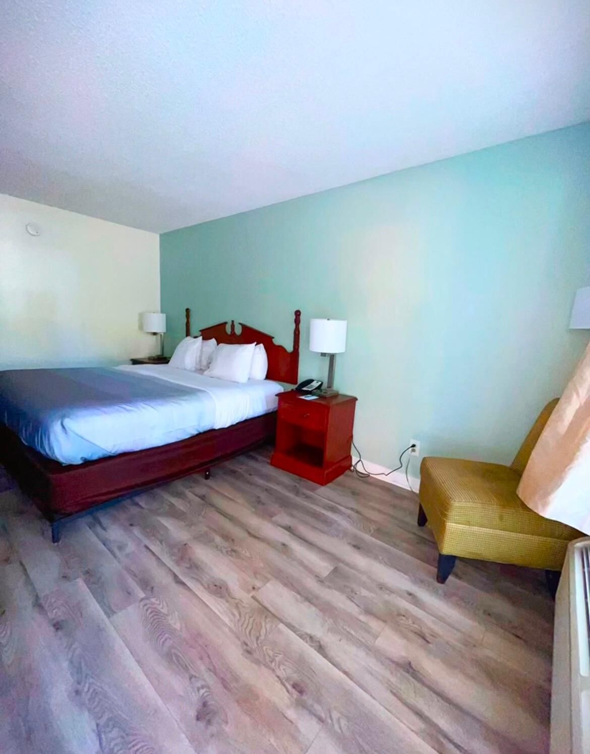 Ein Hotelzimmer mit Bett, Nachttischen, einem Sessel und Holzboden.