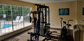 Une salle de sport équipée de matériel d’exercice, une piscine et une vue sur la verdure.