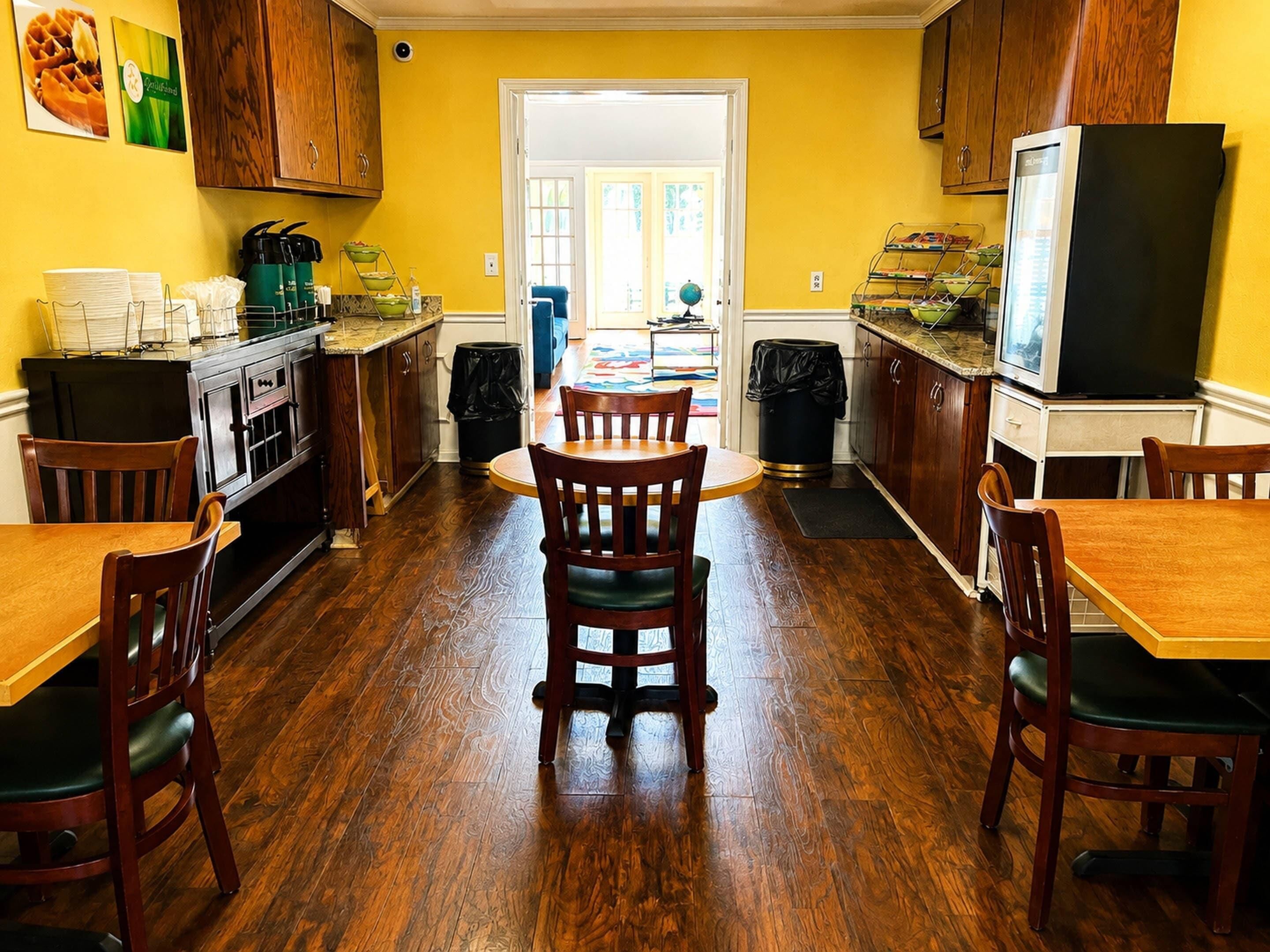 A kitchen with wooden cabinets, a dining table, chairs, and a refrigerator.