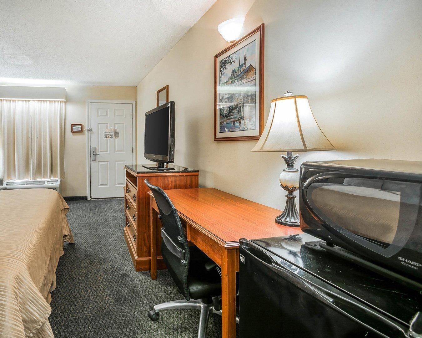 Une chambre d’hôtel avec un lit, un bureau, une télévision, une lampe et un tableau encadré au mur.