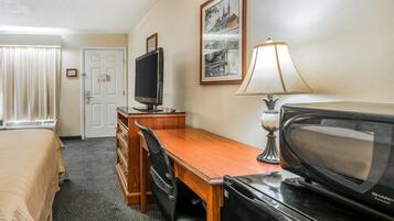 Une chambre d’hôtel avec un lit, un bureau, une télévision, une lampe et un tableau encadré au mur.