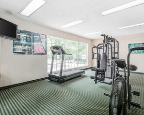 Un gimnasio con cinta de correr, máquinas de pesas y un espejo grande.