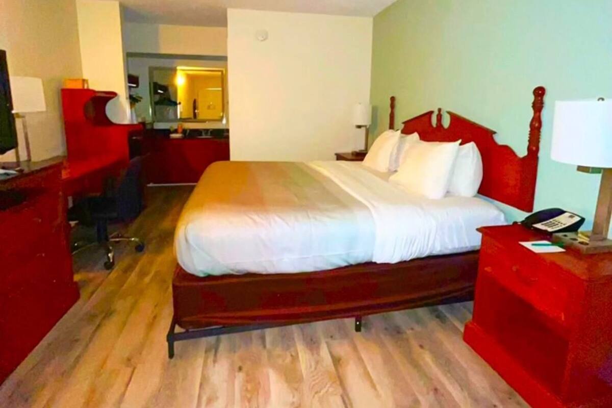 A hotel room with a wooden bed, a desk, a chair, and a small table with a lamp.