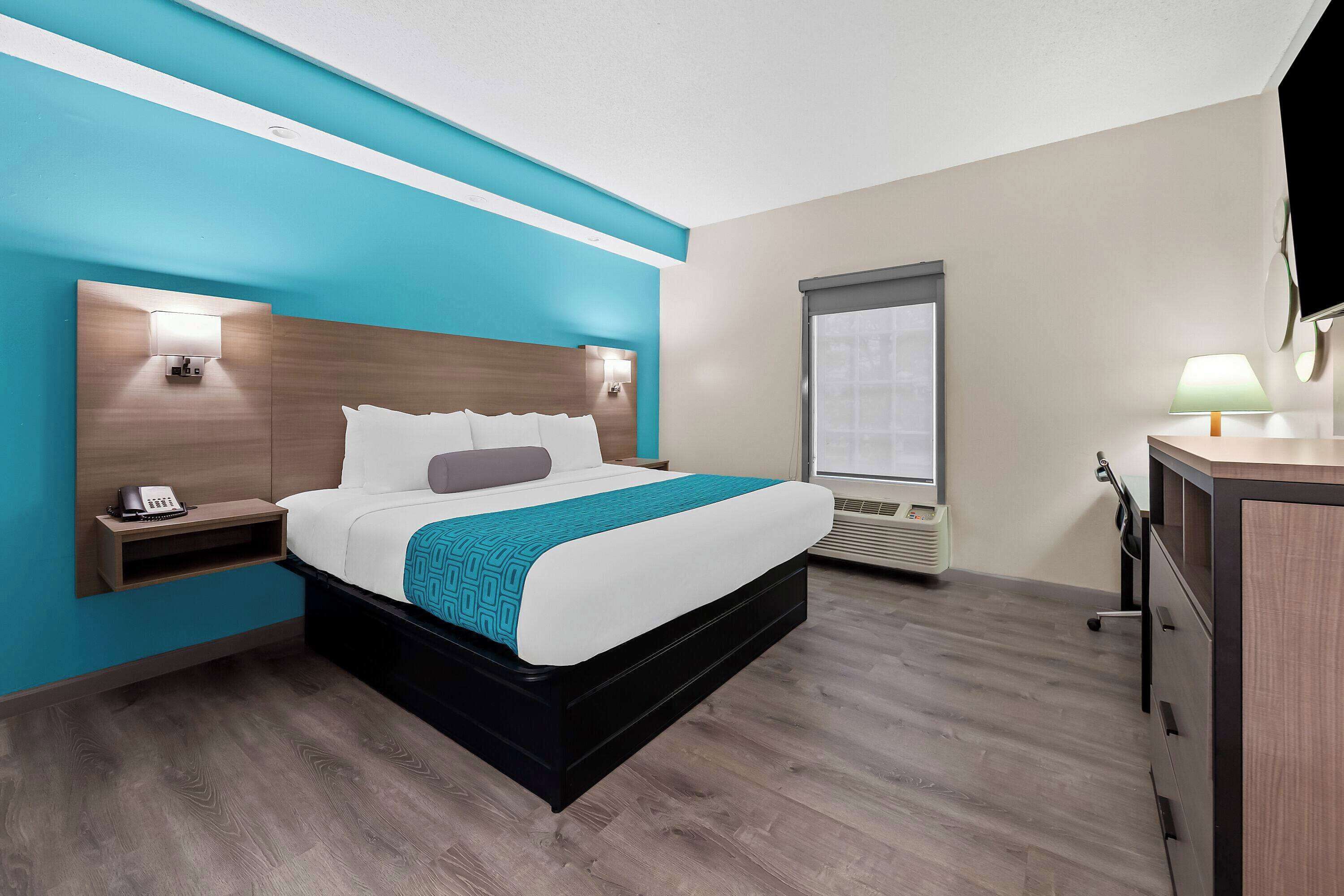 A modern hotel room with a bed, bedside tables, a desk, and a television.