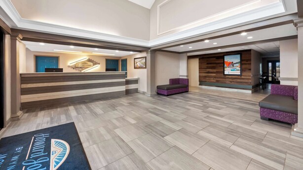 Vestíbulo de hotel con mostrador de recepción, zonas de estar y una pared de madera con cuadros enmarcados.