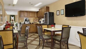 A dining area with wooden chairs and a table, a kitchen with wooden cabinets and appliances, and a mounted flat-screen TV on the wall. - Baymont by Wyndham Eufaula (Eufaula)