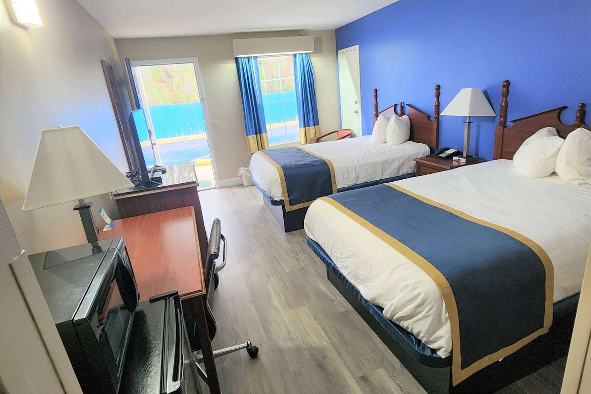 A hotel room with two beds, a desk, a chair, a TV, and a window with curtains.