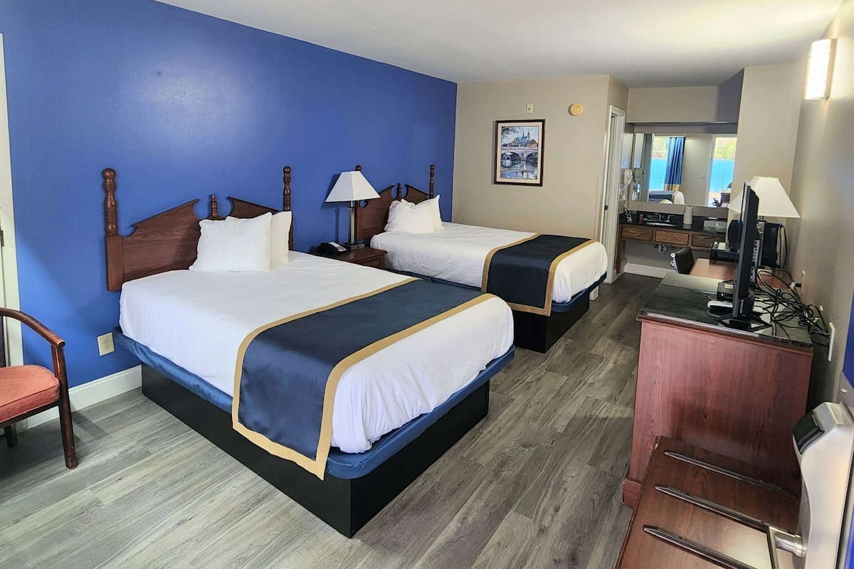 A hotel room with two beds, a desk, a chair, and a mirror.