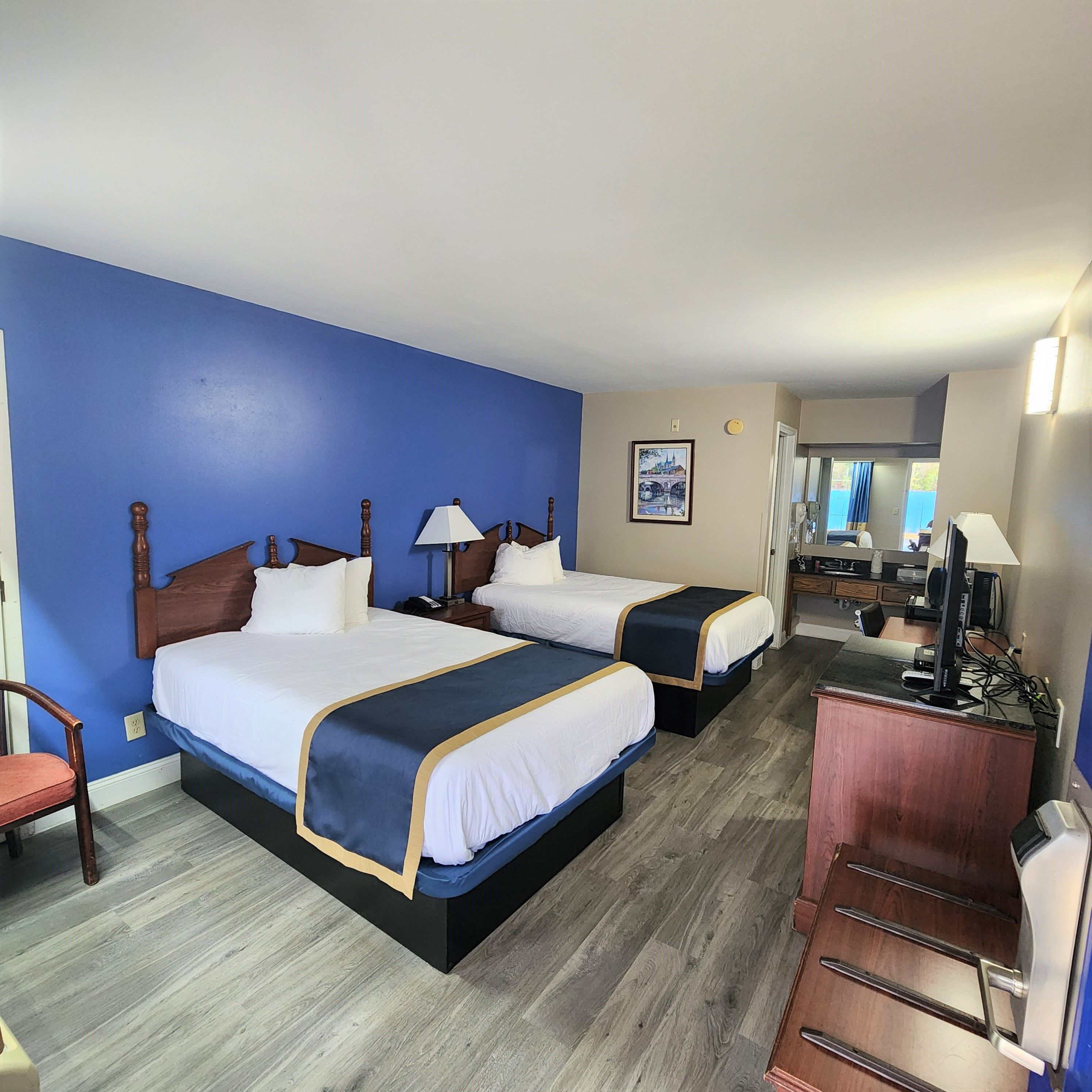 A hotel room with two beds, a desk, a chair, and a television.