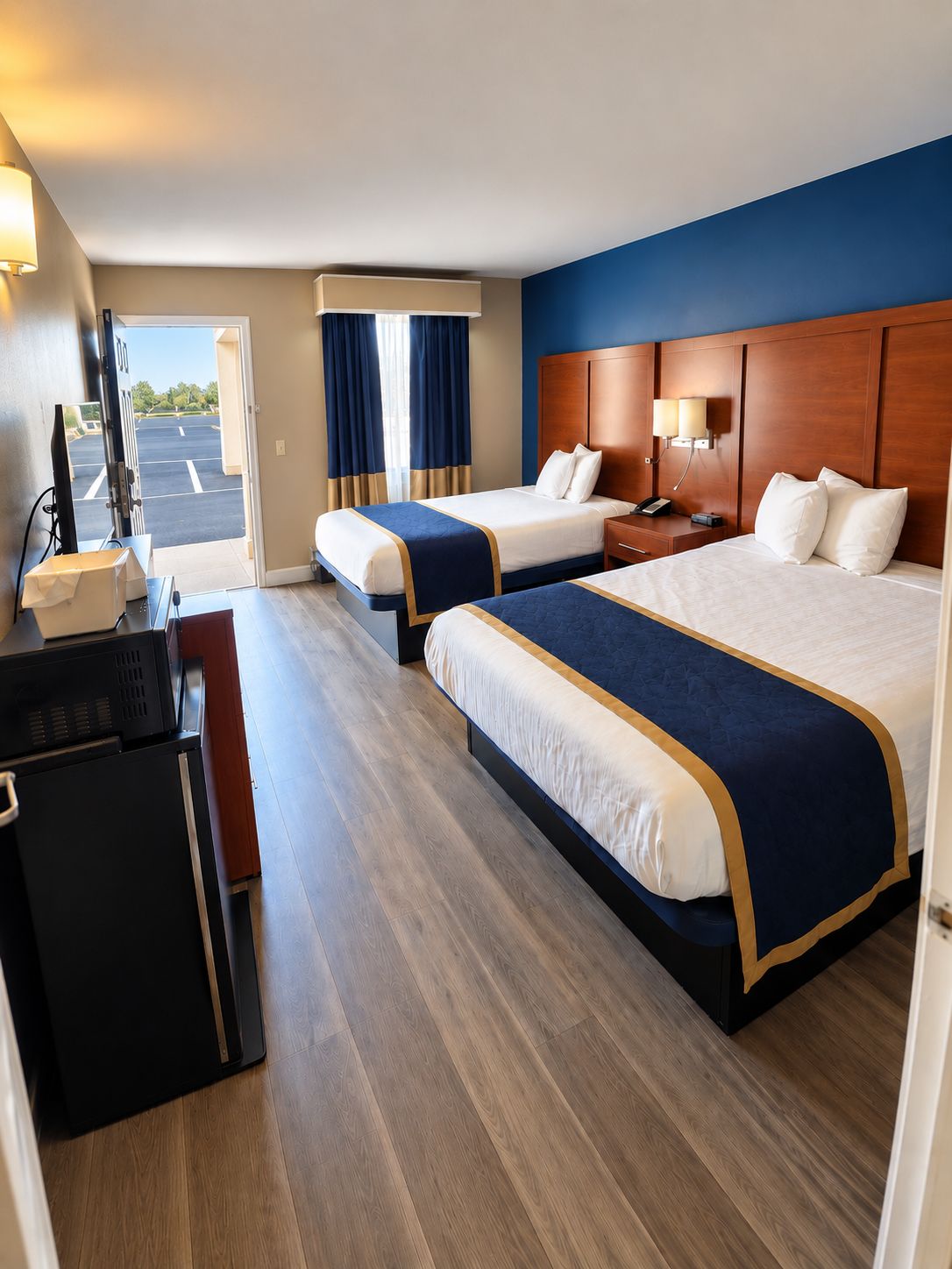 Habitación de hotel con dos camas, un escritorio, un televisor y vista a un estacionamiento.