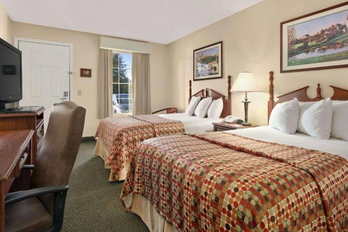 A hotel room with two beds, a desk, a chair, a television, and a window with curtains.