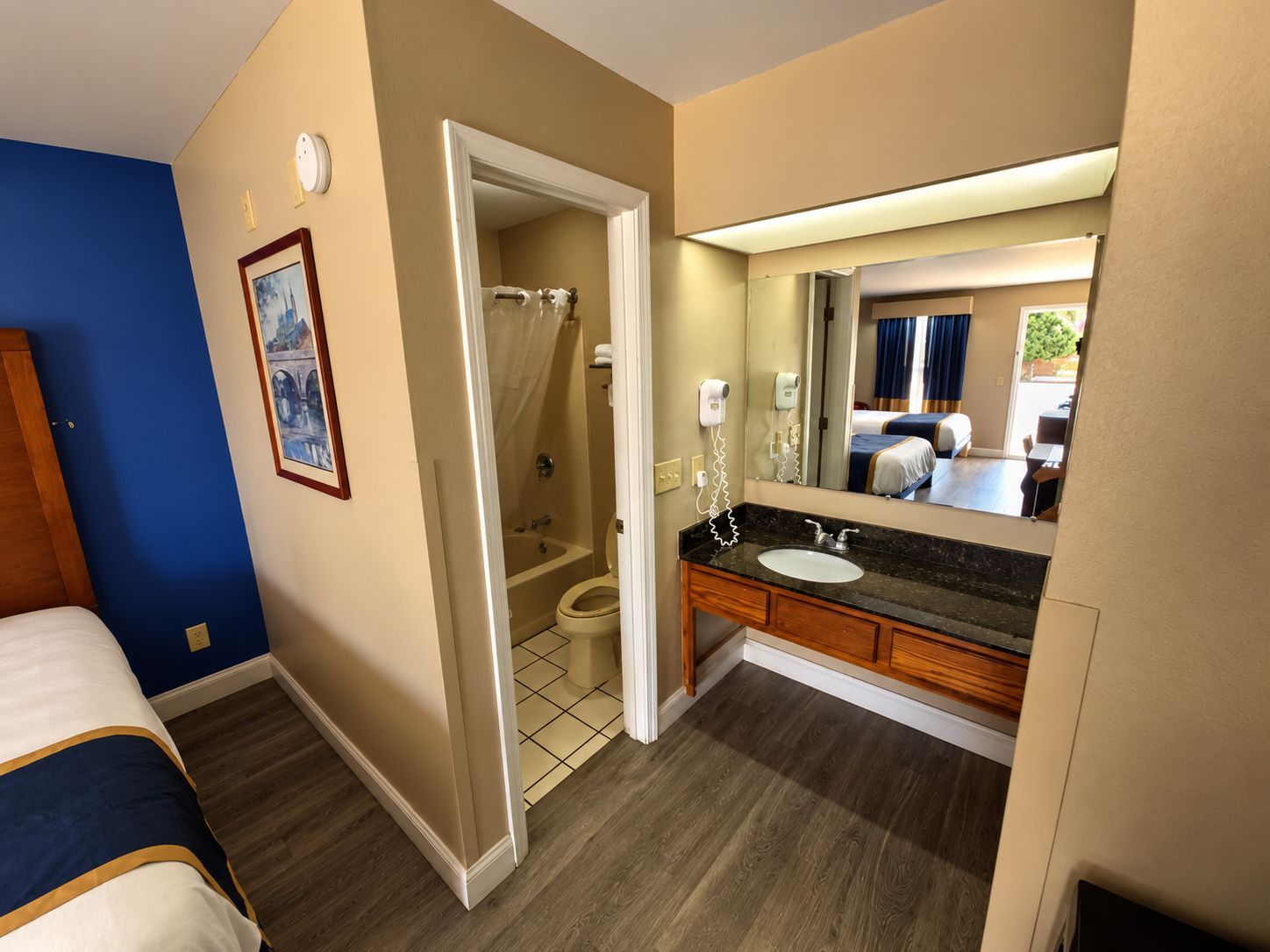 Une chambre d’hôtel avec une douche, un lit, une salle de bain avec un lavabo et un miroir, et une vue sur l’extérieur.