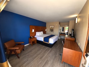 A hotel room with a bed, a desk, a chair, and a bathroom visible through an open door.
