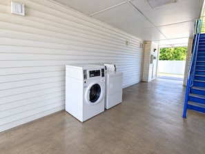 Een wasruimte met een wasmachine en droger, een blauwe handgreep en een witte buitenmuur.