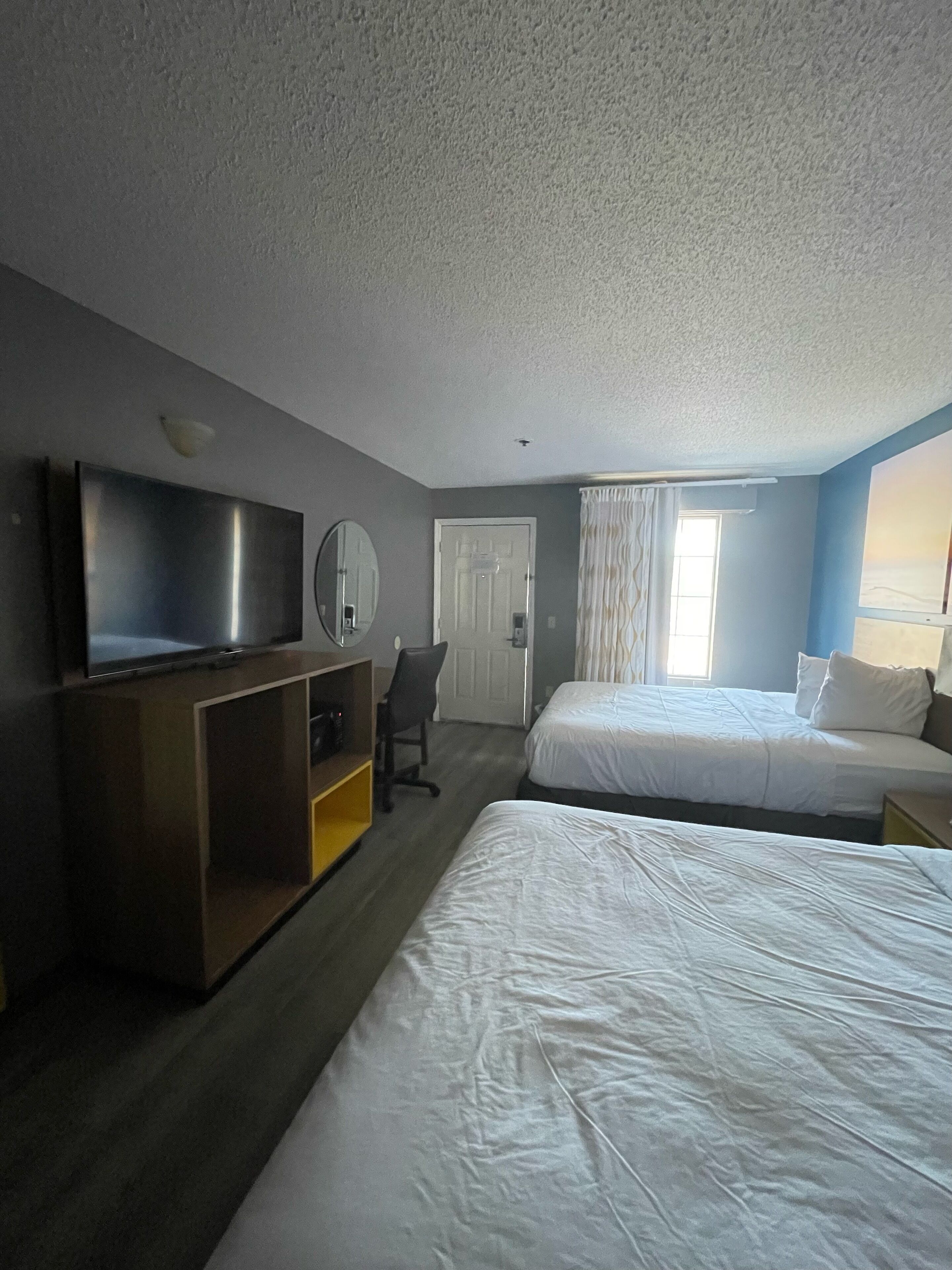 A hotel room with two beds, a TV, a desk with a chair, and a door.