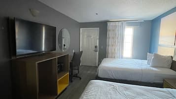A hotel room with two beds, a TV, a desk with a chair, and a door.