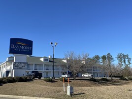 Un Baymont Inn & Suites con un letrero grande, un estacionamiento y un edificio con techo verde.