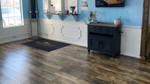 Een ruime kamer met houten vloer, een groot raam, een receptiebalie, een televisie en een spiegel.