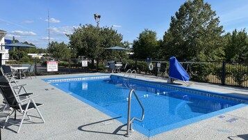 Una piscina con quiosco de salvavidas, sillas junto a la piscina y una tumbona cubierta.