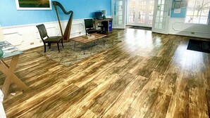 Een ruime kamer met houten vloer, een bureau met computer, een stoel en een harp.