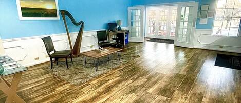 A spacious room with a wooden floor, a desk with a computer, a chair, and a harp.