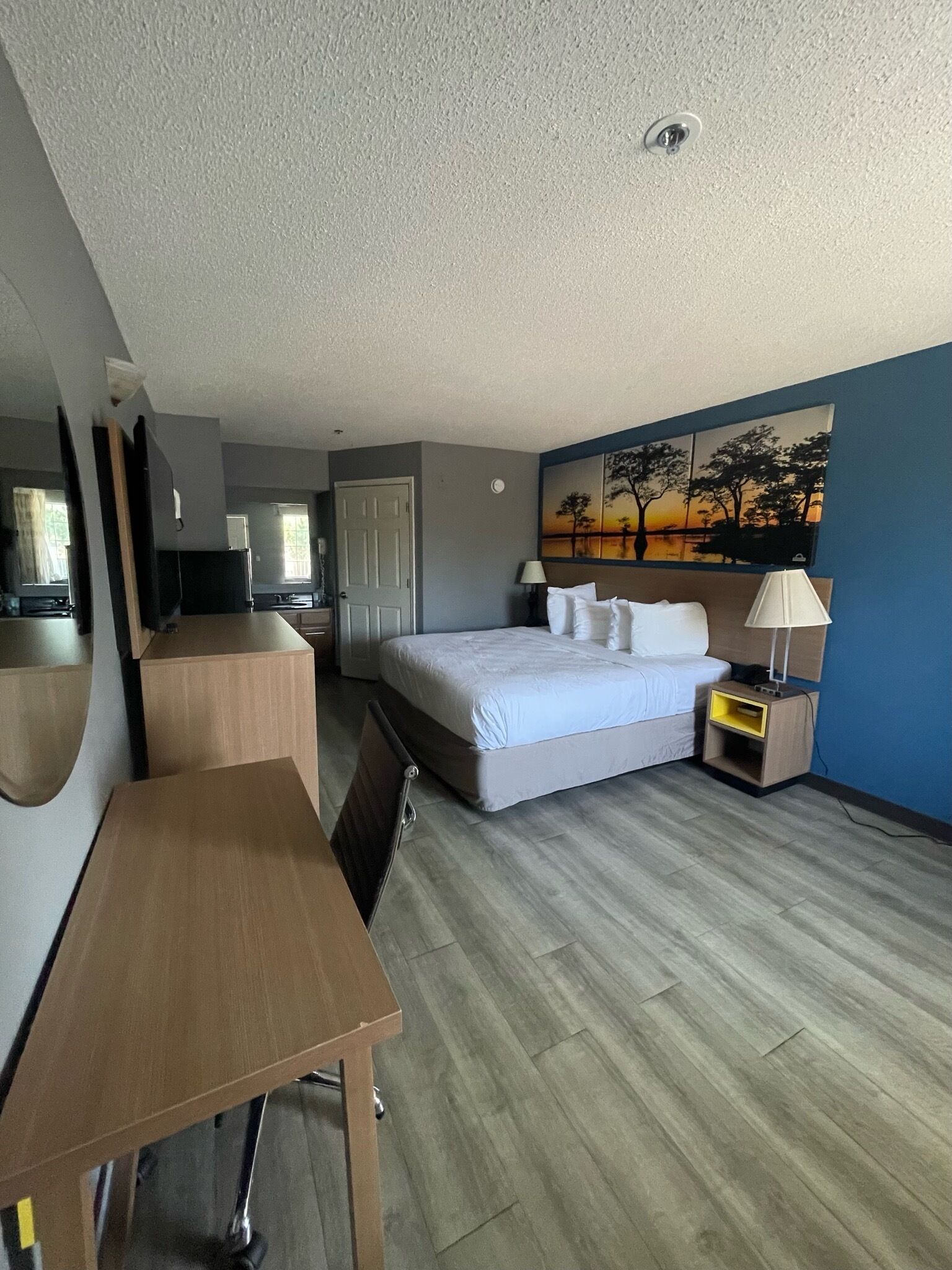 Una habitación de hotel con cama, mesita de noche, lámpara y un cuadro en la pared.