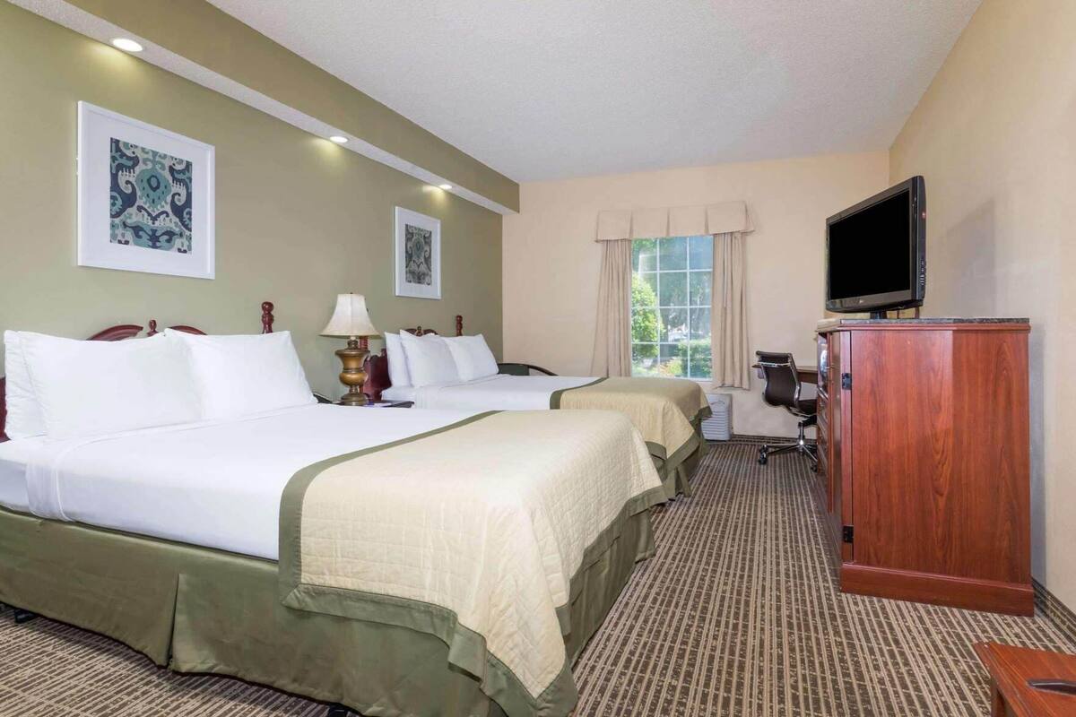 A hotel room with two beds, a television, a desk, and a window with curtains.