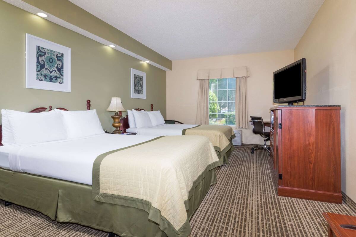A hotel room with two beds, a television, a desk, and a window with curtains.