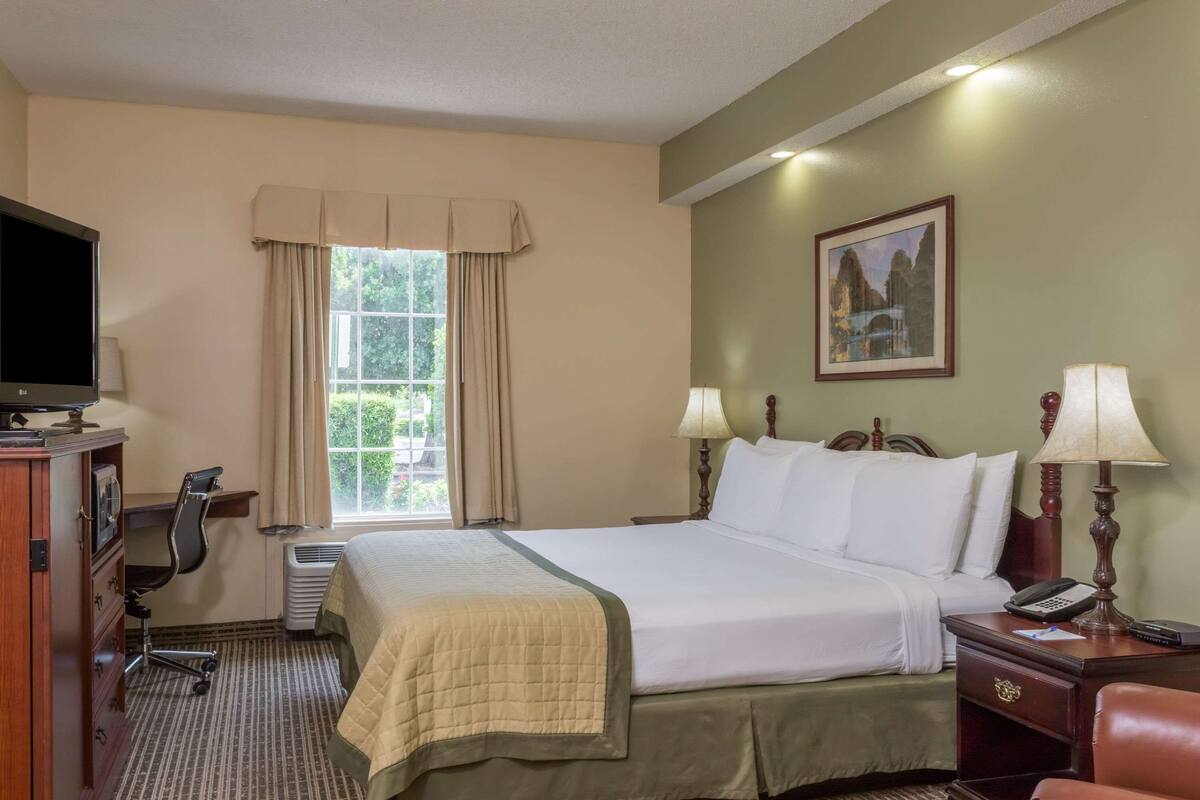 A hotel room with a bed, bedside lamps, a desk with a chair, a television, and a window with curtains.