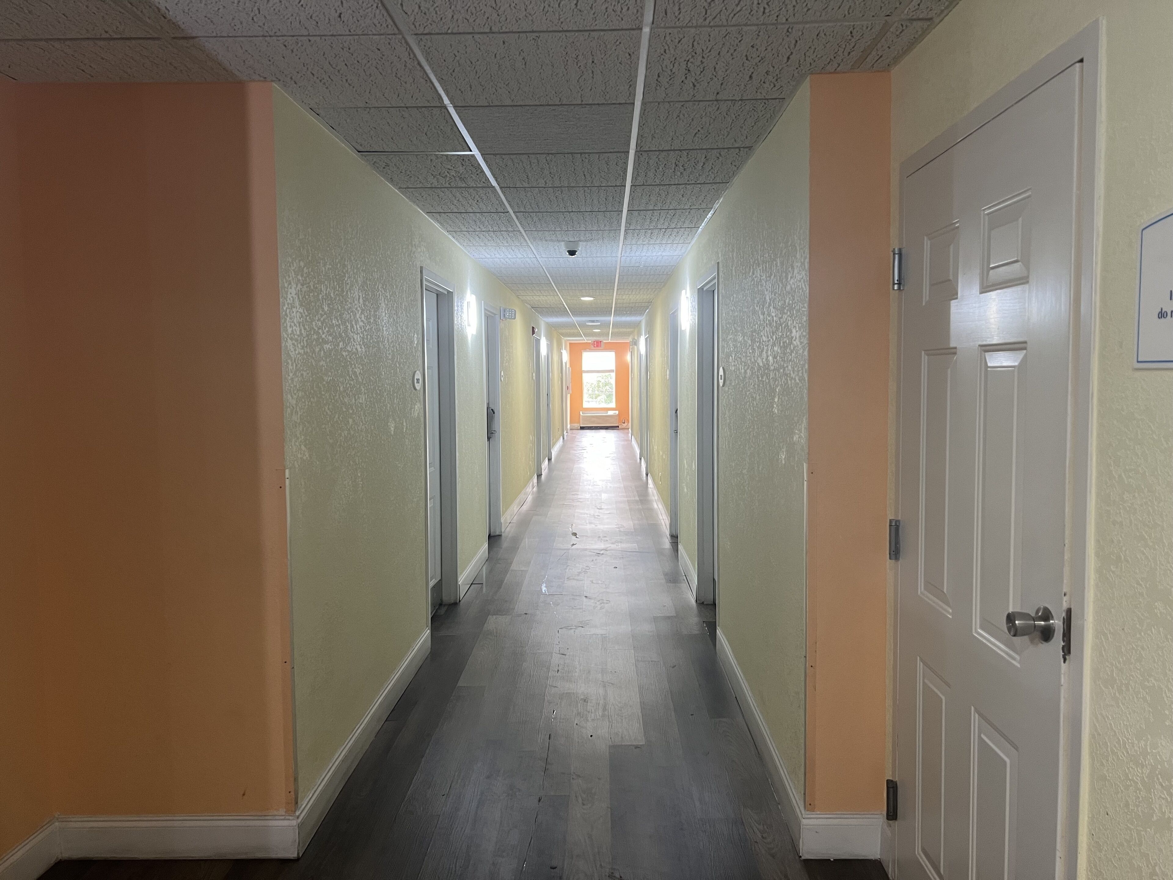 A long, narrow hallway with doors on both sides, leading to a bright room at the end.