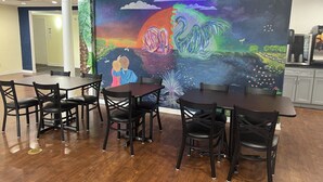 A dining area with wooden tables and chairs, a large mural on the wall depicting a vibrant landscape with a swan, and a view of the adjacent room.